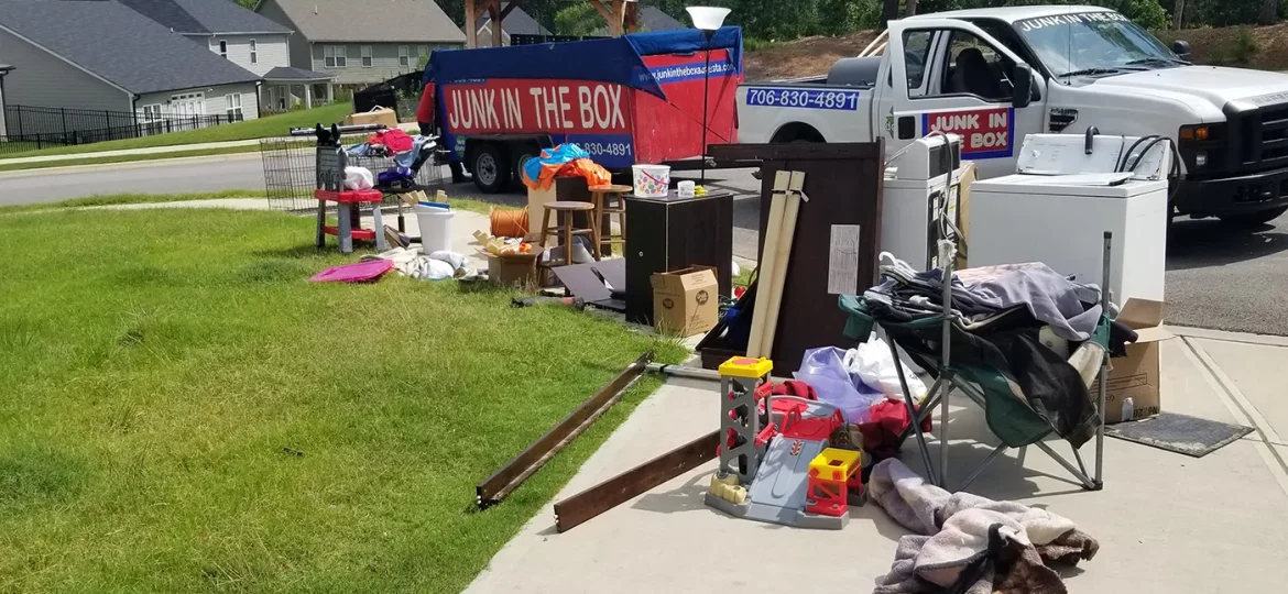 front yard of a home with indoor junk items laying in the grass in front of dumpster