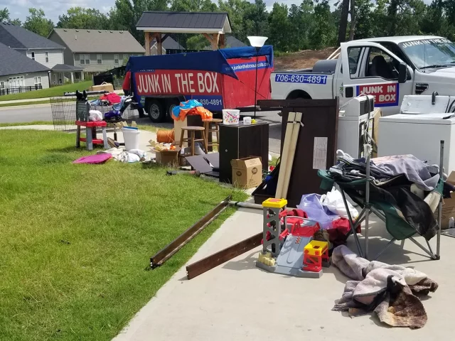 front yard of a home with indoor junk items laying in the grass in front of dumpster
