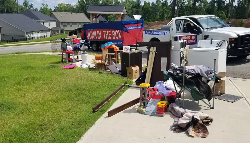 front yard of a home with indoor junk items laying in the grass in front of dumpster