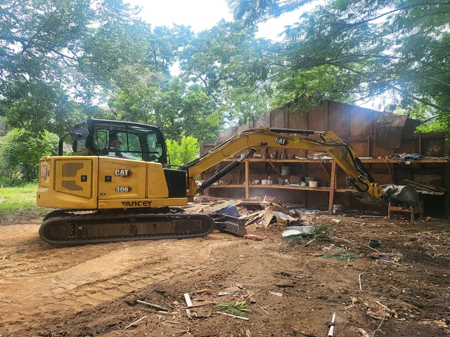 Excavator tearing down a dilapidated storage building for demolition