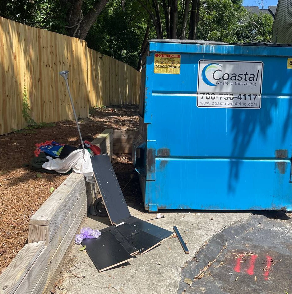 Junk cluttering up the curb by a dumpster.